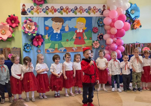 Dzieci stoją na tle dekoracji, gości wita Wojtek przebrany za Krasnala Hałabałę