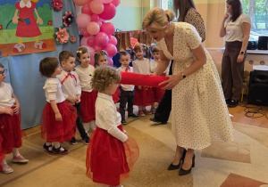 Pani dyrektor pasuje przedszkolaki duzżym ołówkiem.