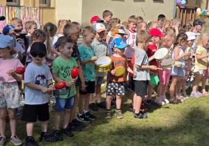 Przedszkolaki trzymają instrumenty muzyczne w rękach i śpiewają piosenki dla rodziców.