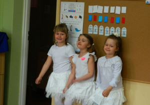 Trzy dziewczynki w białych strojach w oczekiwaniu na występ.