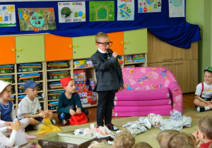 Chłopiec w za dużych okularach recytuje wiersz.
