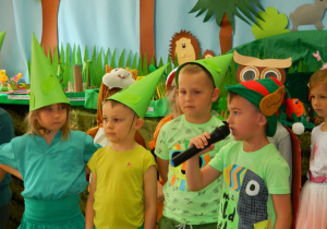 Dzieci przebrane za skrzaty leśne mówią wiersze do mikrofonu.