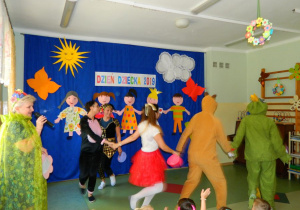 Rodzice i nauczyciele trzymjąc się za ręce tańczą dla dzieci.