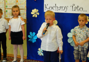 Chłopiec w w stroju galowym mówi wiersz przez mikrofon.