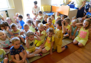 Dzieci z grupy Jeżyków siedzą na dywanie i słuchają zagadek.