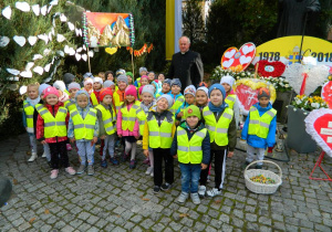 Przedszkolaki przed pomnikiem Jana Pawła II z księdzem 