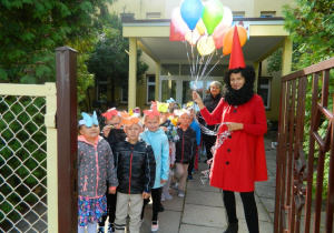 Krasnal Hałabała stoi wraz z dziećmi w wejściu do przedszkola z balonami w ręku.