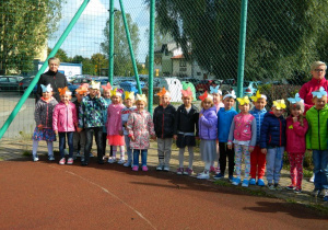 Dzieci z grupy Motylków stoją na boisku obok przedszkola.