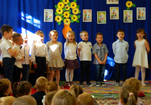 Stojące dzieci na tle dekoracji śpiewają piosenkę.