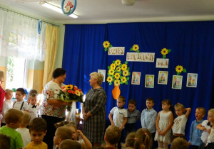 Pani Monika wręcza kwiaty pani Dyerktor stojącej wśród dzieci.