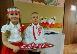 Dziewczynka i chłopiec z grupy Motylków w strojach biało-czerwonych witają gości.
