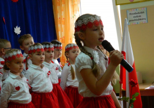 Dziewczynka w stroju biało- czerwonym śpiewa piosenkę.