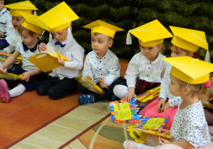 Dzieci siedzą na dywanie i oglądaja dyplomy.