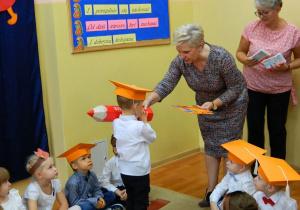 Pani dyrektor pasuje chłopca czerwonym ołówkiem na przedszkolaka.