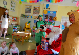 Mikołaj z pomocnikami pokazuje dzieciom przyniesione prezenty.