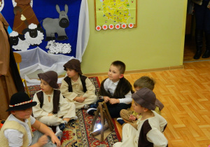 Chłopcy pasterze siedzą na dywanie i śpiewają kolędy