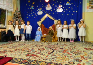Aniołki, świ,eta rodzina i dzieci z grupy Biedronek stoją na tle dekoracji.
