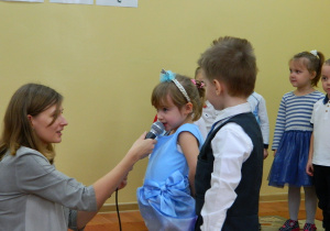 Natalia z pomocą wychowawczyni mówi wiersz do mikrofonu.