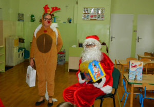 Mikołaj z reniferem pokazują dzieciom prezenty