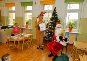 Mikołaj z reniferem pokazują dzieciom prezenty