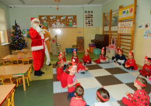 Dzieci siedzą na dywanie, Mikołaj stoi przed nimi i rozmawiają