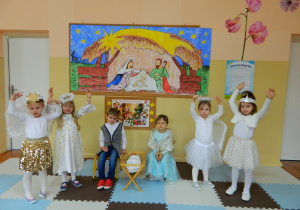 Dziewczynki w przebraniach aniołków śpiewają kolędę dla Jezusa