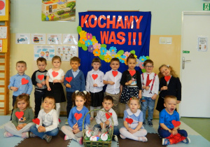 Zdjęcie dzieci z grupy Biedronek na tle dekoracji, trzymają w rączkach czerwone serca