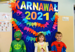 Dzieci w przebraniach spidermana, księżniczki i dinozaura stoją na tle dekoracji