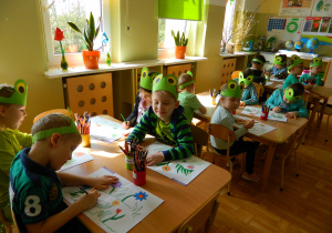 Dzieci siedzą przy stolikach i kolorują wiosnę