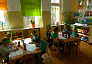 Dziewczynki i chłopcy w opaskach żabek siedzą przy stolikach w sali