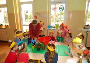 Dzieci siedzą wokół stolika przyglądając się jak pani Lucynka przesadza kwiaty