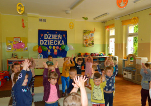 Dziewczynki i chłopcy z najmłodszej grupy klaszczą wysoko unosząc ręce.
