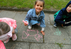 Dziewczynki i chłopcy malują kredą po chodniku