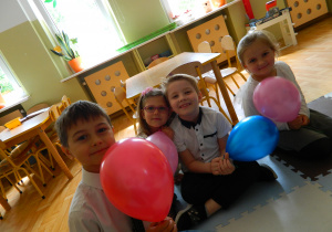 Chłopcy i dziewczynki z grupy Jeżyków siedzą na dywanie z balonami