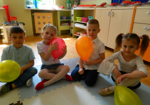 Dzieci z grupy Jeżyków siedzą na dywanie trzymają w rękach balony
