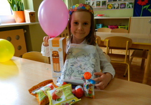 Oliwia siedzi przy stoliku prezentując upominki z okazji Dnia Dziecka