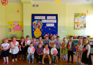 Dzieci z grupy Krasnali trzymają w rękach czerwone serduszka na tle dekoracji