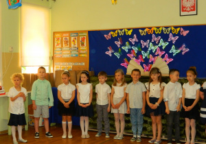 Dzieci z grupy Motylków stoją na tle dekoracji z odfruwających motyli