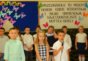 Szymon mówi wiersz do mikrofonu stojąc z dziećmi na środku sali
