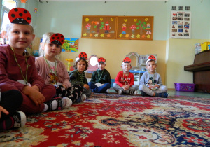 Dzieci w opaskach z emblematem biedronki siedzą na dywanie